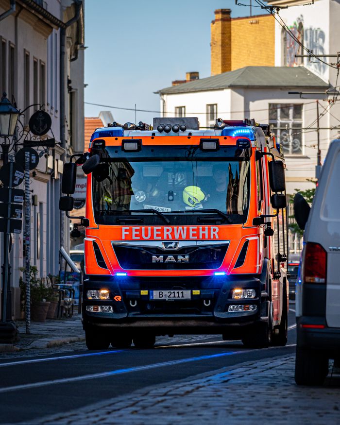 Über Uns A vibrant fire truck marked 'Feuerwehr' navigates through a Berlin street, responding to an emergency.